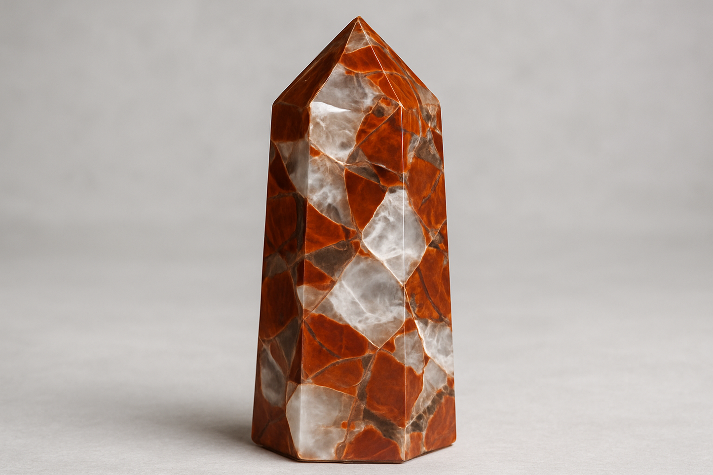 A polished breciated jasper tower crystal with rich reddish-brown colors and prominent clear and white quartz veins running throughout the stone