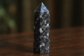 A Yooperlite crystal tower in natural lighting showing its dark gray to black syenite rock with subtle white to gray sodalite inclusions, polished to a high shine
