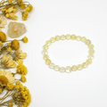 Citrine bracelet flat in circle with pale lemon-yellow translucent round beads and raw citrine cluster props on light grey background