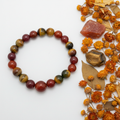 Carnelian and tiger eye bracelet flat in circle with alternating orange-red and golden-brown 10mm beads and raw stone props on light grey background
