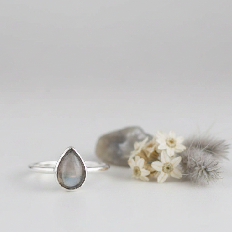 Grey moonstone teardrop sterling silver ring upright with stone facing forward and white grey props on light grey background