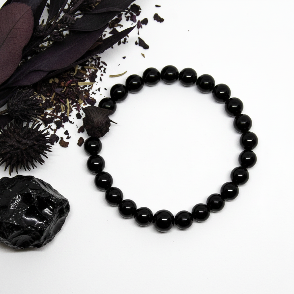 Black obsidian bracelet flat in circle with jet black glossy round beads and raw obsidian chunk props on light grey background