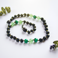 Raw molasses Baltic amber necklace with vivid green aventurine and malachite beads draped in elegant loop on light grey background