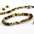 Polished olive mix Baltic amber necklace with alternating lemon-yellow and dark molasses-olive beads draped in elegant loop on light grey background