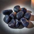 Iolite tumbled stones cluster hero shot — deep dark blue-grey with natural veining in candlelight