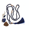 Lapis lazuli and lava stone 108 bead mala with navy silk tassel draped on light grey background
