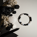Black Obsidian and Moonstone 8mm beaded stretch bracelet with raw obsidian chunk, white flowers and black taper candle on light grey background