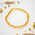 Raw gold Baltic amber necklace with warm golden-yellow matte round beads draped in elegant loop on light grey background