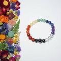 Seven chakra gemstone bracelet flat in circle showing full rainbow of red jasper carnelian citrine aventurine sodalite amethyst clear quartz beads on light grey background