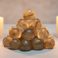 Rutilated quartz tumbled stones cluster hero shot with golden rutile needles in candlelight