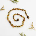 Polished olive Baltic amber necklace with deep olive-green to golden-brown round beads draped in elegant loop on light grey background