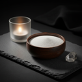 Fine white altar sand in a wooden bowl on dark slate surface with ritual tools