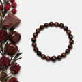 Red Tiger's Eye bracelet flat in circle with deep mahogany-red round beads and silky chatoyant flash on light grey background