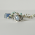 Blue lace agate class ring upright with ornate silver filigree setting and pale blue banded oval stone on light grey background