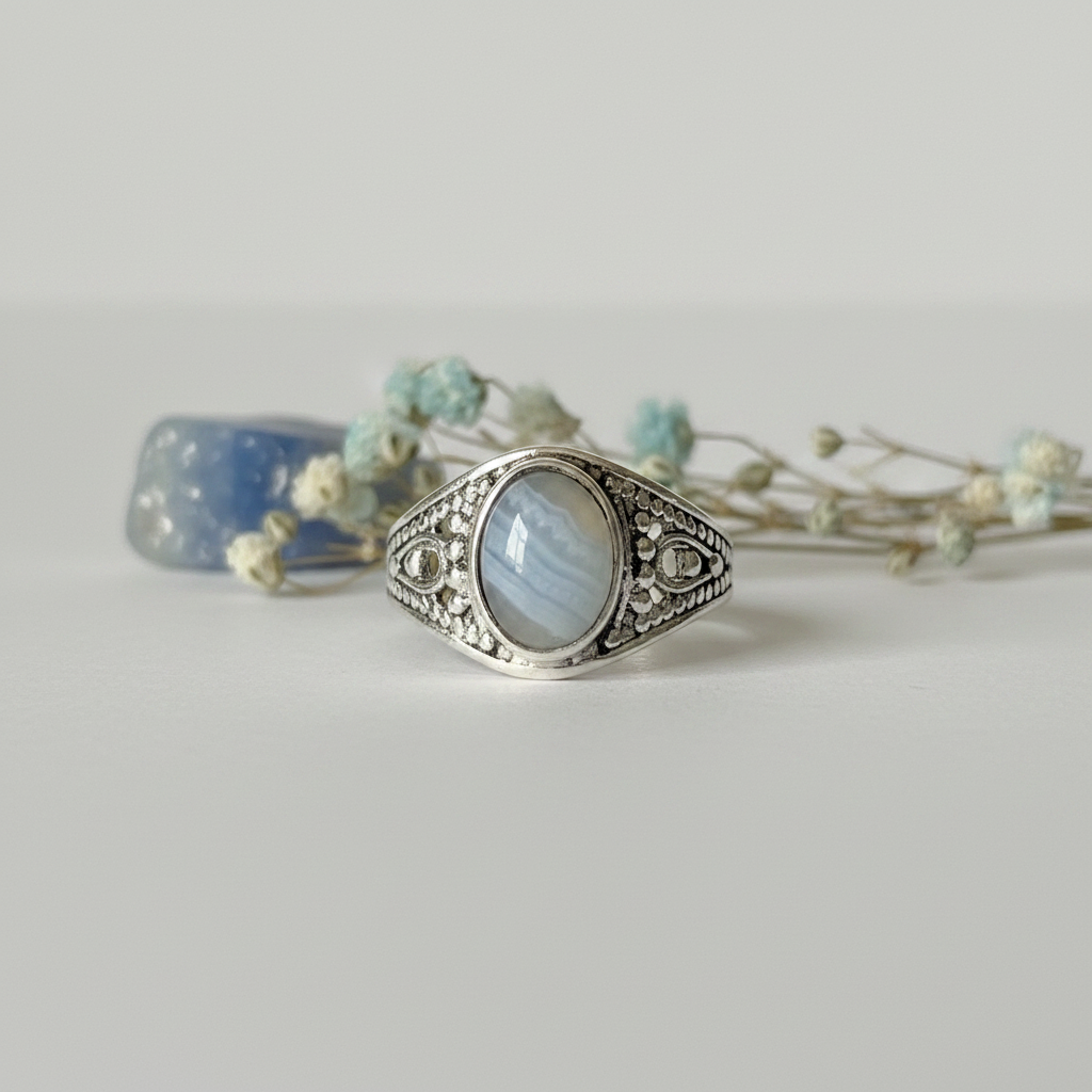 Blue lace agate class ring upright with ornate silver filigree setting and pale blue banded oval stone on light grey background